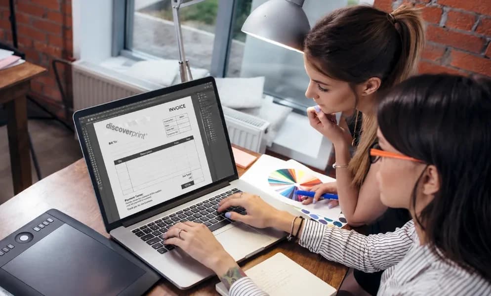 Two designers setting an invoice book design on screen